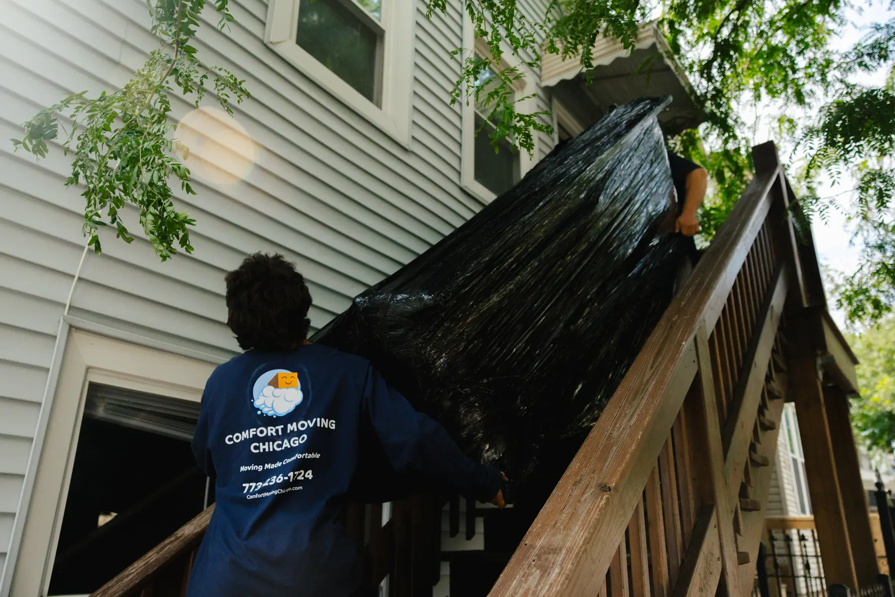 Comfort Moving Chicago crew carrying a wrapped sofa on rear apartment stairs